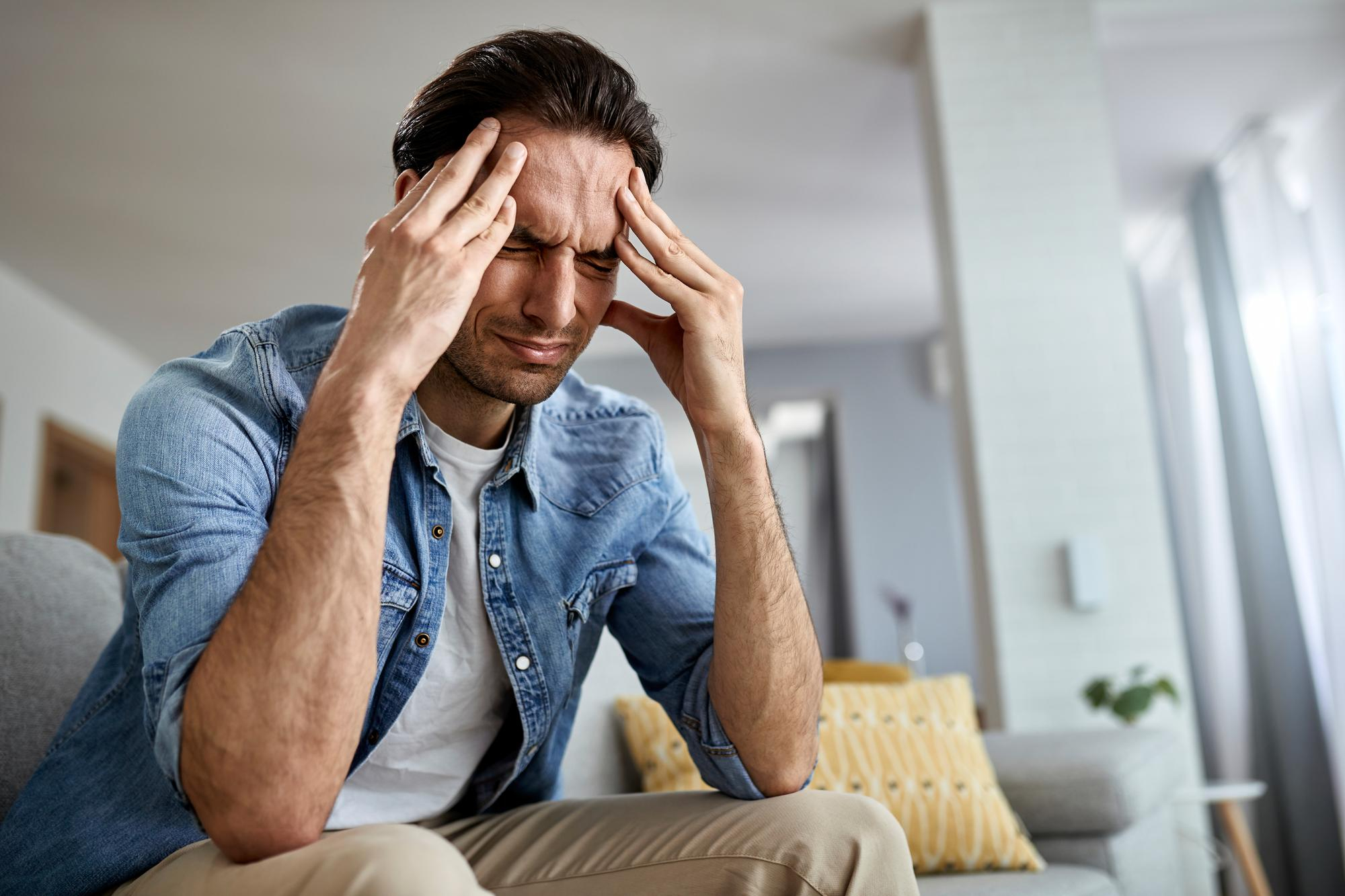 low-angle-view-distraught-man-holding-his-head-pain-while-sitting-living-room